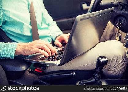 transport, business trip, technology and people concept - close up of young man with laptop computer driving car