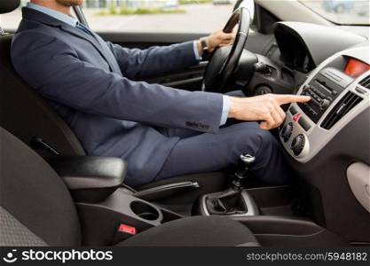 transport, business trip, technology and people concept - close up of young man in suit driving car and adjusting music volume on control panel stereo system