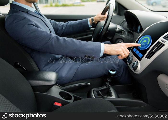 transport, business trip, technology and people concept - close up of young man in suit driving car and adjusting car eco mode system settings on dashboard computer screen