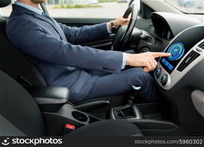 transport, business trip, technology and people concept - close up of young man in suit driving car and adjusting car eco mode system settings on dashboard computer screen