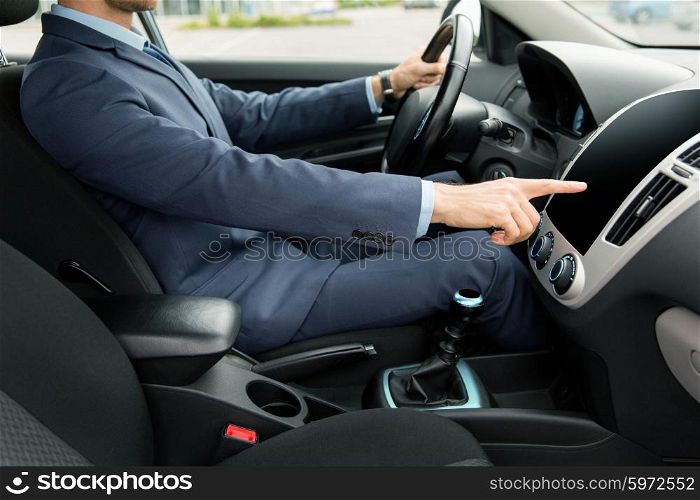 transport, business trip, technology and people concept - close up of young man in suit driving car and pointing finger to blank black computer screen on dashboard