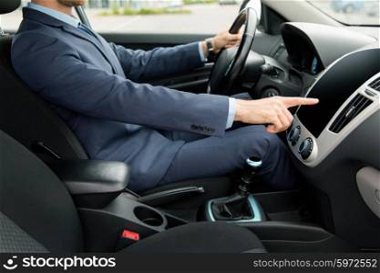 transport, business trip, technology and people concept - close up of young man in suit driving car and pointing finger to blank black computer screen on dashboard