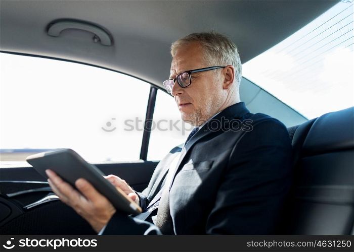 transport, business trip, technology and people concept - senior businessman with tablet pc computer driving on car back seat
