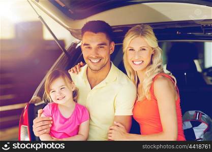 transport, leisure, road trip and people concept - happy family with little girl sittin on open hatchback car trunk at home parking space