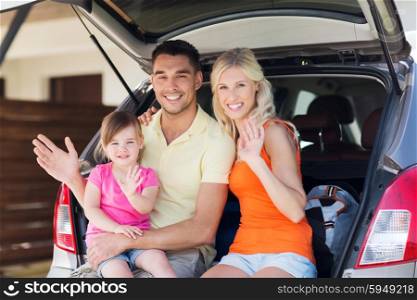 transport, leisure, road trip and people concept - happy family with little girl sitting on trunk of hatchback car and waving hands at home parking space