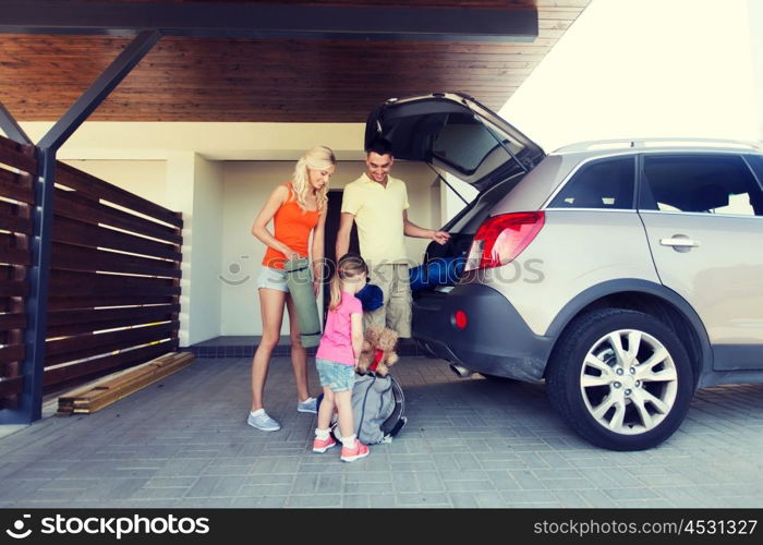 transport, leisure, travel, road trip and people concept - happy family packing things into car at home parking