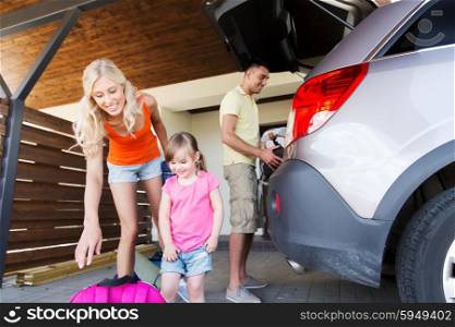 transport, leisure, travel, road trip and people concept - happy family packing things into car at home parking
