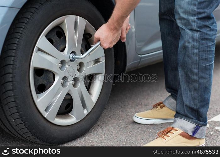 transport, repair, maintenance and people concept - close up of man with wrench changing car tire