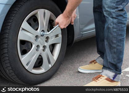 transport, repair, maintenance and people concept - close up of man with wrench changing car tire