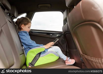 transport, road trip, travel, technology and people concept - happy little girl with tablet pc driving in car safety seat