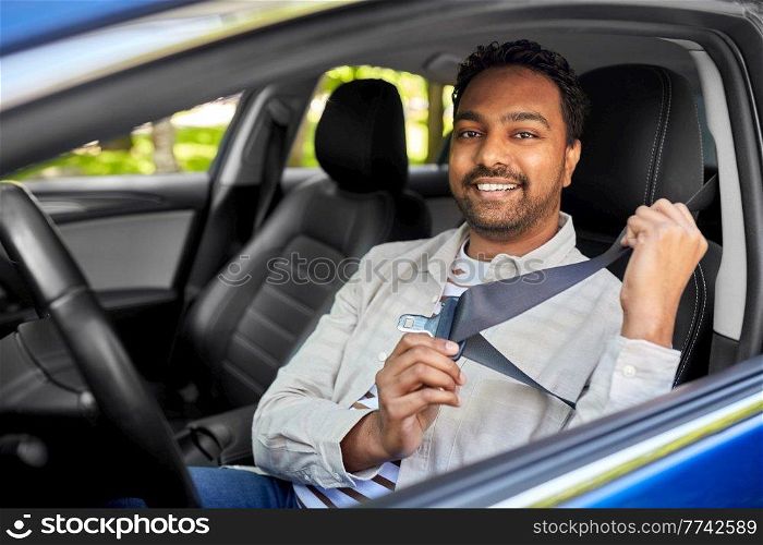 transport, safety and people concept - happy smiling indian man or driver fastening seat belt in car. smiling indian driver fastening seat belt in car