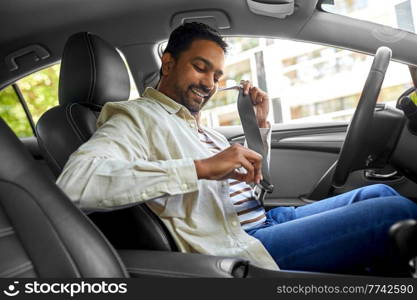 transport, safety and people concept - happy smiling indian man or driver fastening seat belt in car. smiling indian driver fastening seat belt in car