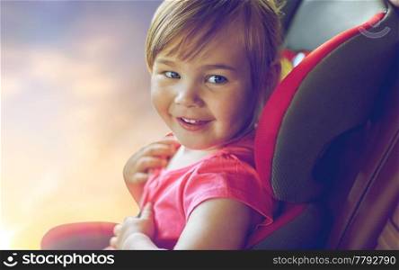 transport, safety, road trip and childhood concept - close up of happy little girl sitting in baby car seat over evening sky background. close up of little girl sitting in baby car seat