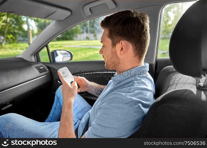 transport, taxi and communication concept - smiling male passenger using smartphone on back seat of taxi car. male passenger using smartphone in taxi car