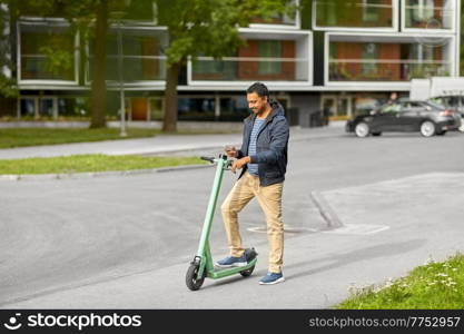 transport, technology and people and concept - happy smiling young man with electric scooter using smartphone on city street. man with smartphone and electric scooter in city