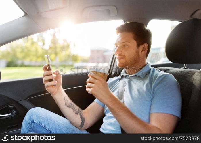 transport, technology and people concept - male passenger drinking coffee and using smartphone on back seat of taxi car. passenger drinking coffee using smartphone in car