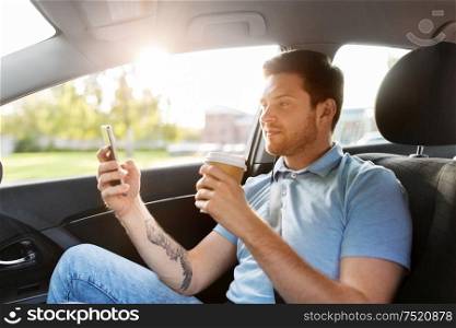 transport, technology and people concept - male passenger drinking coffee and using smartphone on back seat of taxi car. passenger drinking coffee using smartphone in car