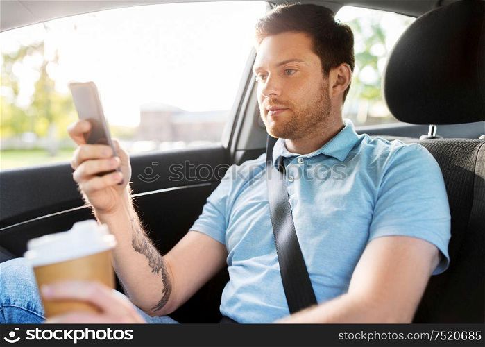 transport, technology and people concept - male passenger with coffee using smartphone on back seat of taxi car. passenger with coffee using smartphone in taxi car