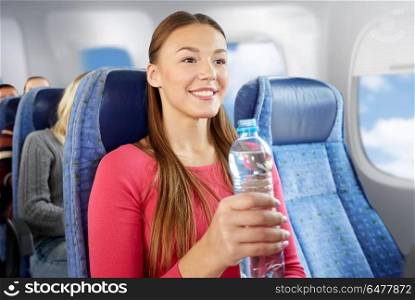 transport, tourism and people concept - happy young woman with water bottle in plane over porthole background. happy young woman with water bottle in plane. happy young woman with water bottle in plane
