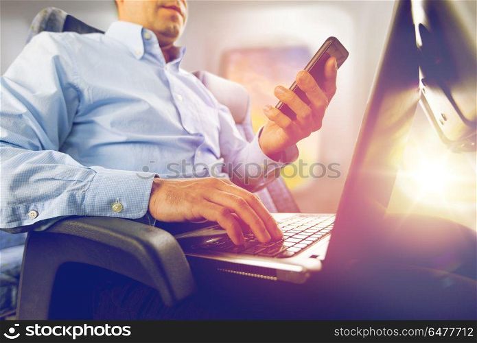 transport, tourism and technology concept - close up of businessman with smartphone and laptop traveling by plane and working over porthole background. businessman with smartphone and laptop in plane. businessman with smartphone and laptop in plane