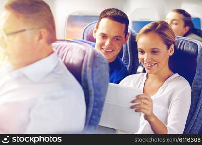 transport, tourism and technology concept - happy passengers or tourists with tablet pc computer in plane over porthole background. happy passengers with coffee talking in plane. happy passengers with coffee talking in plane