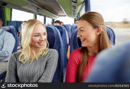transport, tourism, friendship, road trip and people concept - happy young women sitting and talking in travel bus