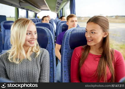 transport, tourism, friendship, road trip and people concept - happy young women sitting and talking in travel bus