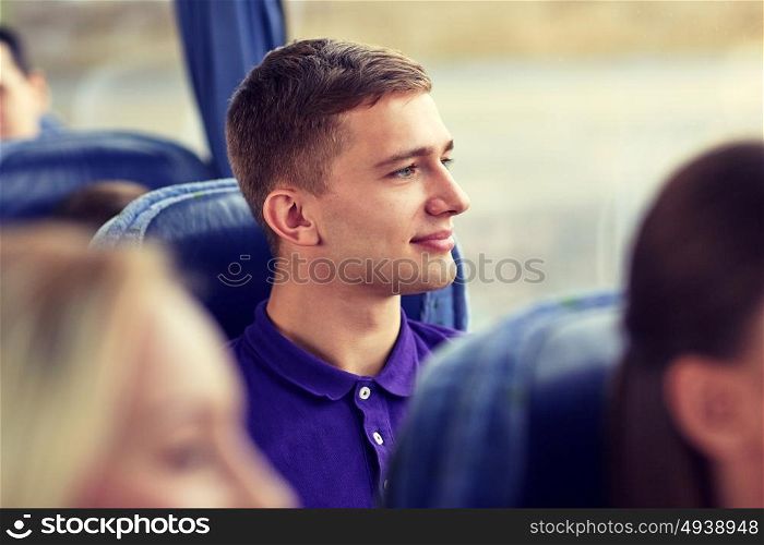 transport, tourism, road trip and people concept - happy young man sitting in travel bus and looking through window. happy young man sitting in travel bus