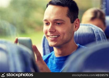 transport, tourism, road trip and people concept - happy young man sitting in travel bus or train with smartphone. happy man sitting in travel bus with smartphone