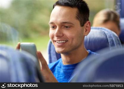 transport, tourism, road trip and people concept - happy young man sitting in travel bus or train with smartphone