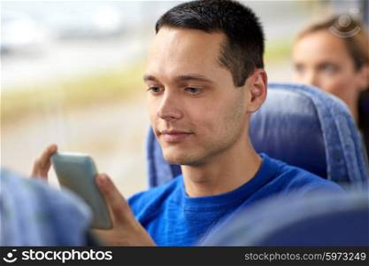 transport, tourism, road trip and people concept - happy young man sitting in travel bus or train with smartphone