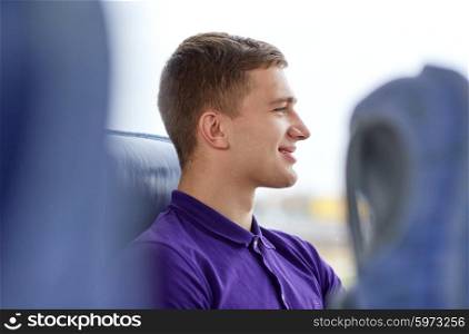 transport, tourism, road trip and people concept - happy young man sitting in travel bus or train and looking through window