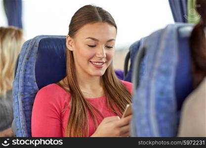 transport, tourism, road trip and people concept - happy young woman sitting in travel bus with smartphone