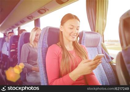 transport, tourism, road trip and people concept - happy young woman sitting in travel bus with smartphone