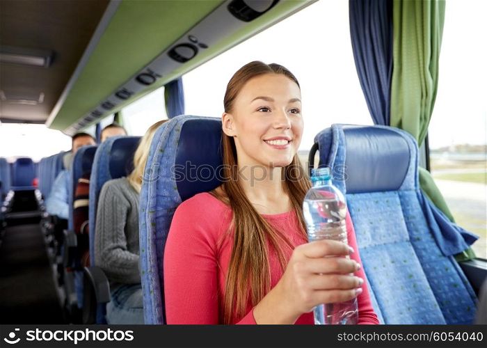 transport, tourism, road trip and people concept - happy young woman with water bottle in travel bus