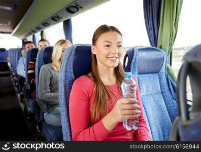 transport, tourism, road trip and people concept - happy young woman with water bottle in travel bus