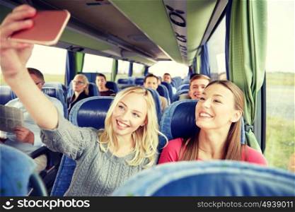 transport, tourism, road trip and people concept - happy young women or friends in travel bus taking selfie by smartphone. women taking selfie by smartphone in travel bus