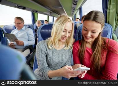 transport, tourism, road trip and people concept - happy young women or friends in travel bus texting or reading message on smartphone