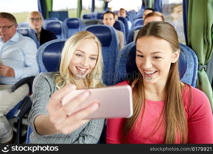 transport, tourism, road trip and people concept - happy young women or friends in travel bus taking selfie by smartphone