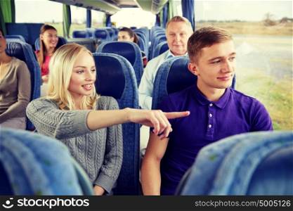 transport, tourism, road trip and people concept - young couple with group of tourists driving in travel bus and pointing finger to something outside. group of tourists in travel bus
