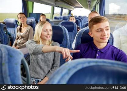 transport, tourism, road trip and people concept - young couple with group of tourists driving in travel bus and pointing finger to something outside