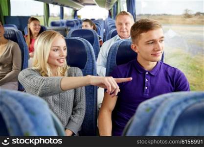 transport, tourism, road trip and people concept - young couple with group of tourists driving in travel bus and pointing finger to something outside