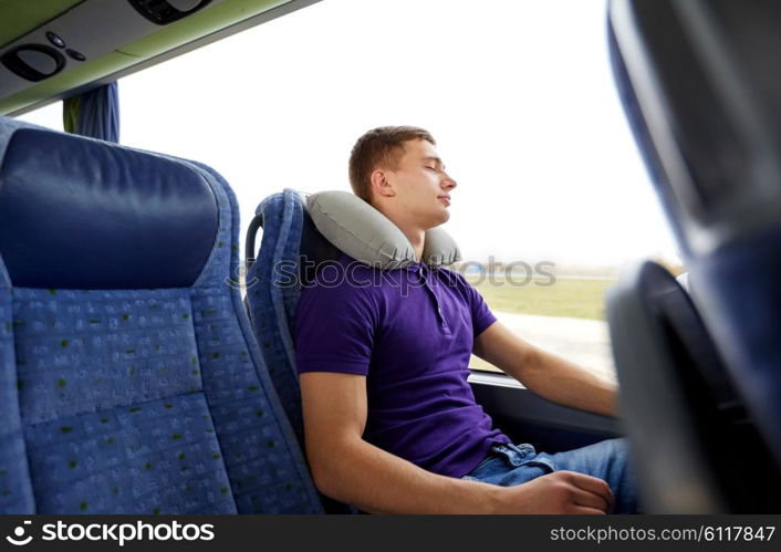 transport, tourism, road trip, rest and people concept - happy young man sleeping in travel bus with inflatable pillow