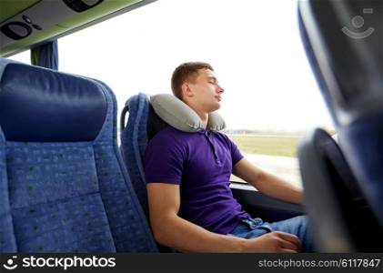 transport, tourism, road trip, rest and people concept - happy young man sleeping in travel bus with inflatable pillow
