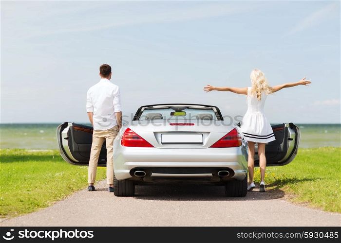 transport, travel, road trip and people concept - happy man and woman near cabriolet car at sea side