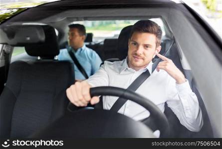 transport, vehicle and people concept - male driver with wireless earphones or hands free device driving car with passenger. male driver with wireless earphones driving car