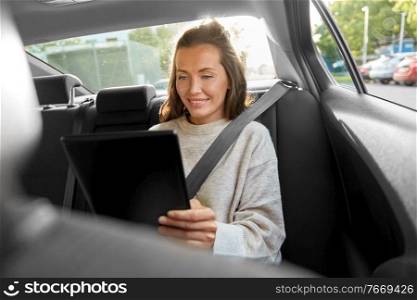 transport, vehicle and technology concept - happy smiling woman or female passenger in taxi car using tablet pc computer. happy smiling woman in car using tablet computer