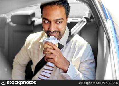 transportation and people concept - happy smiling indian man with takeaway coffee on back seat in taxi car. indian man with takeaway coffee on car back seat