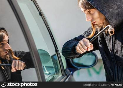 Transportation, crime and ownership concept - Male hooded thief burglar breaking smashing the car window.. Thief burglar breaking smashing the car window