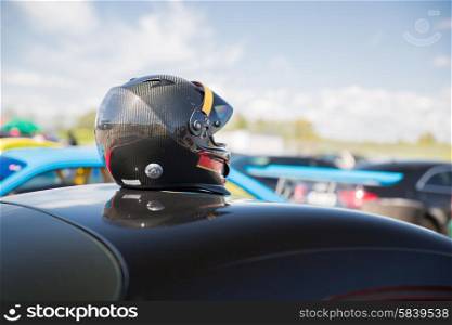 transportation, high speeds, racing and road concept - close up of car on autodrome or parking with helmet on roof top from back
